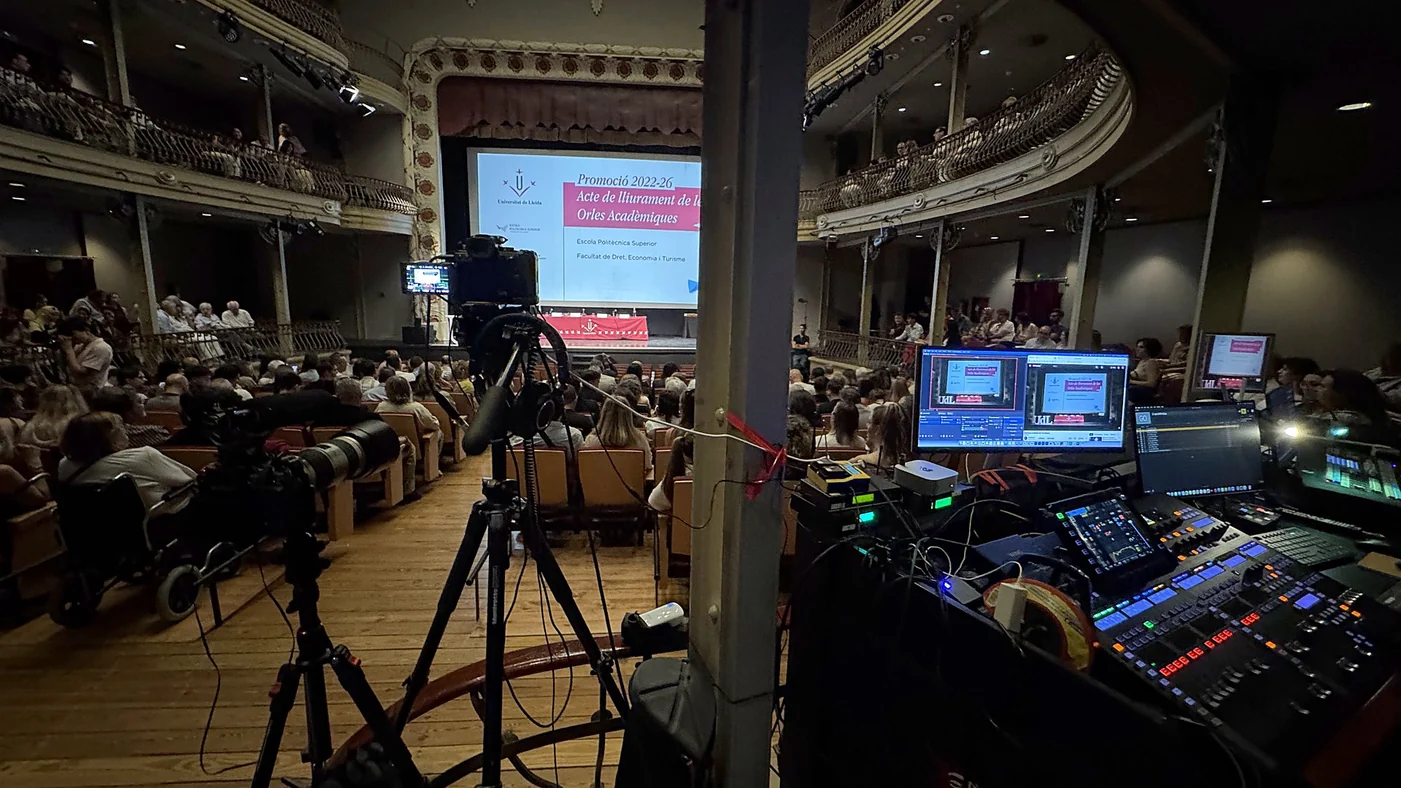 Cámaras sobre trípode y mesa de realización del directo durante un acto de graduación en un teatro