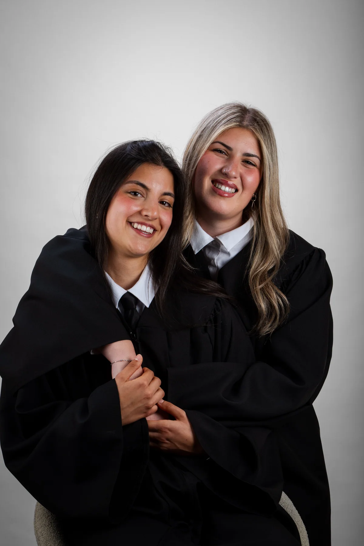 Dos compañeras con toga se abrazan sonriendo en el estudio