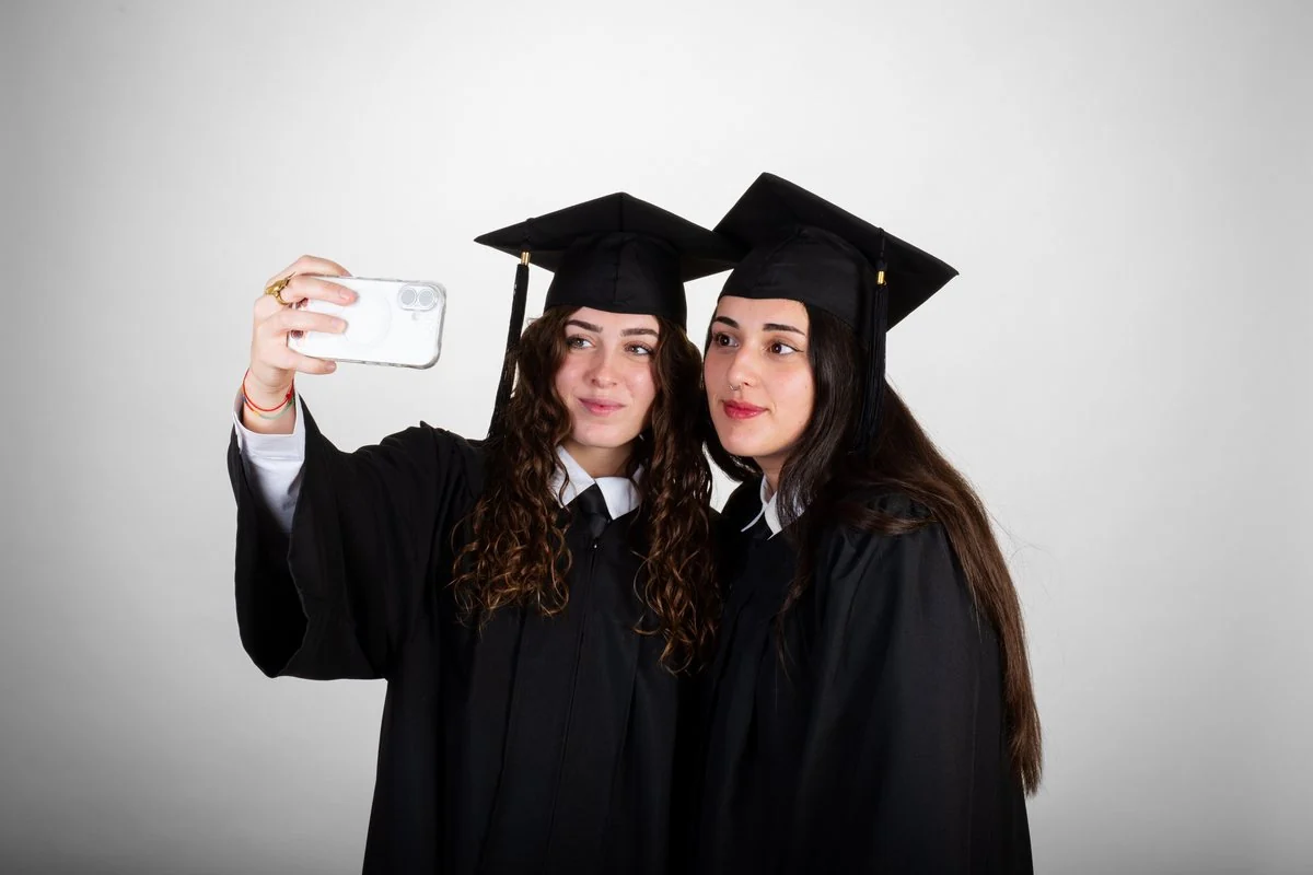 Dos graduadas con birrete se hacen un selfie en el estudio