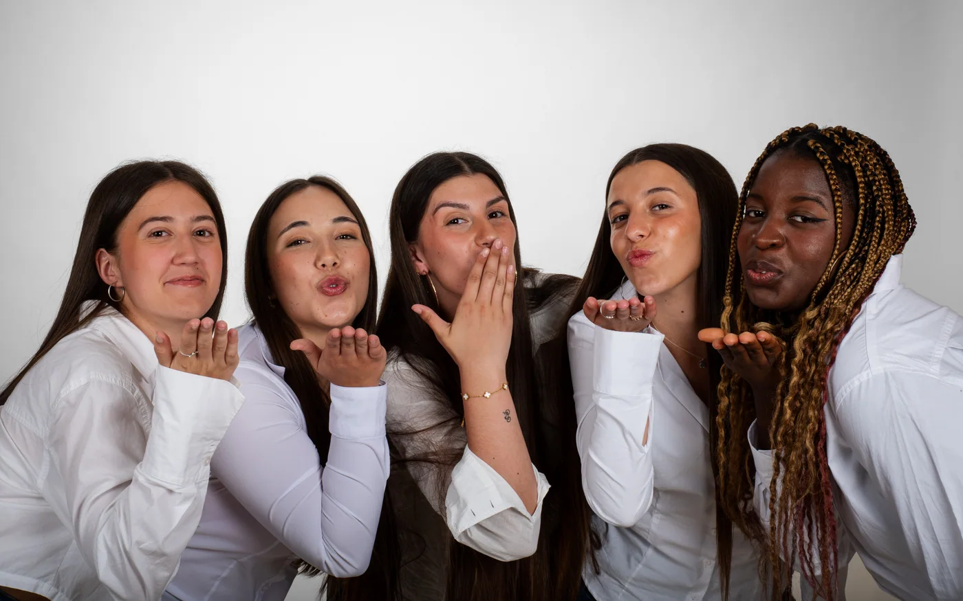Cinco alumnas con camisa blanca lanzan un beso a la cámara en el estudio