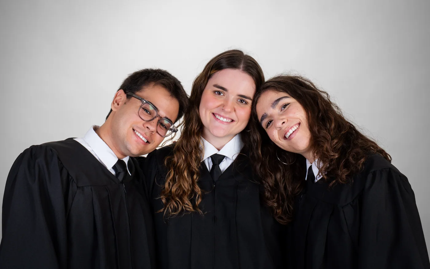 Tres graduados con toga apoyan la cabeza unos en otros y sonríen