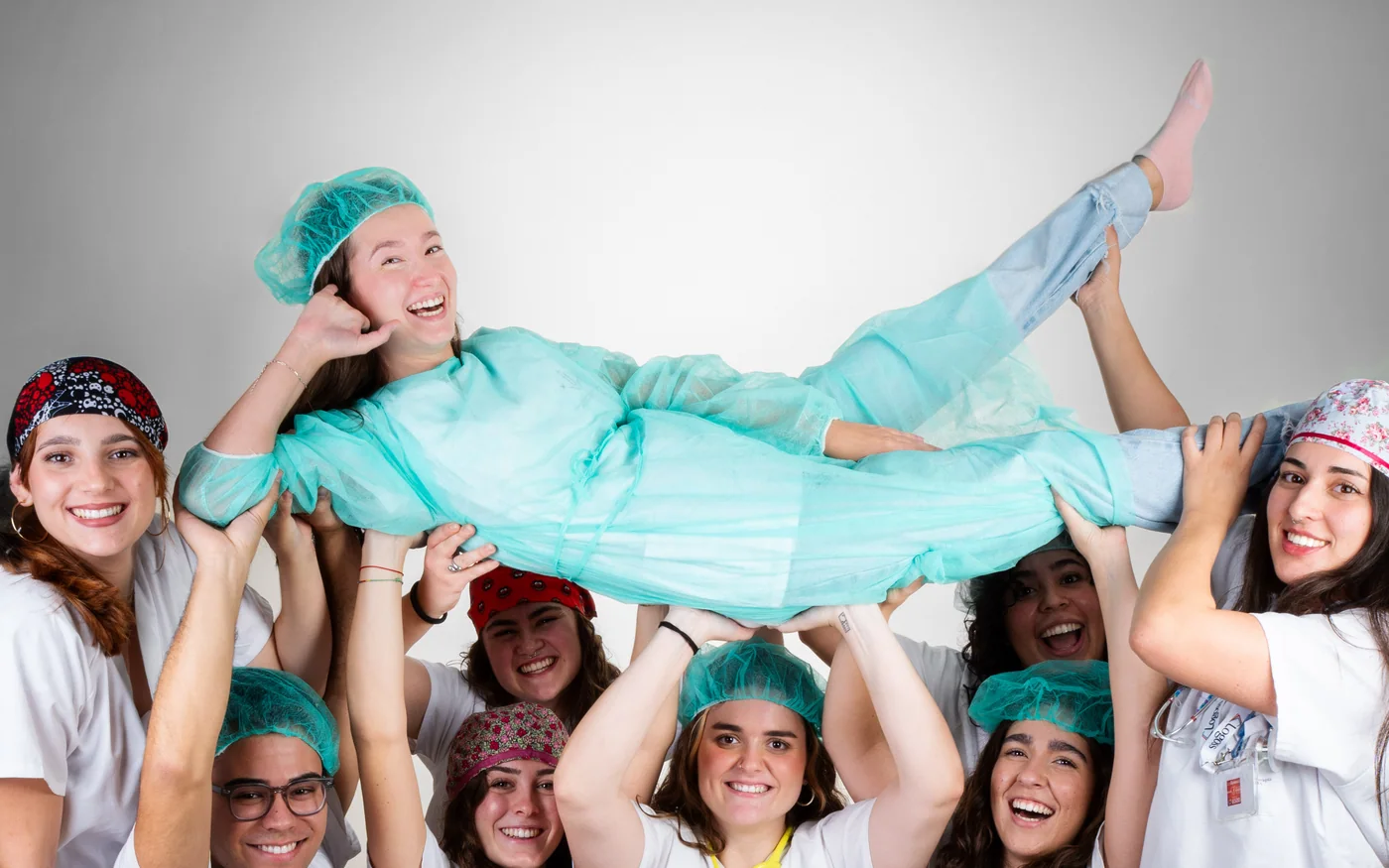 Alumnos de Enfermería con pijama y gorro de quirófano levantan en brazos a una compañera