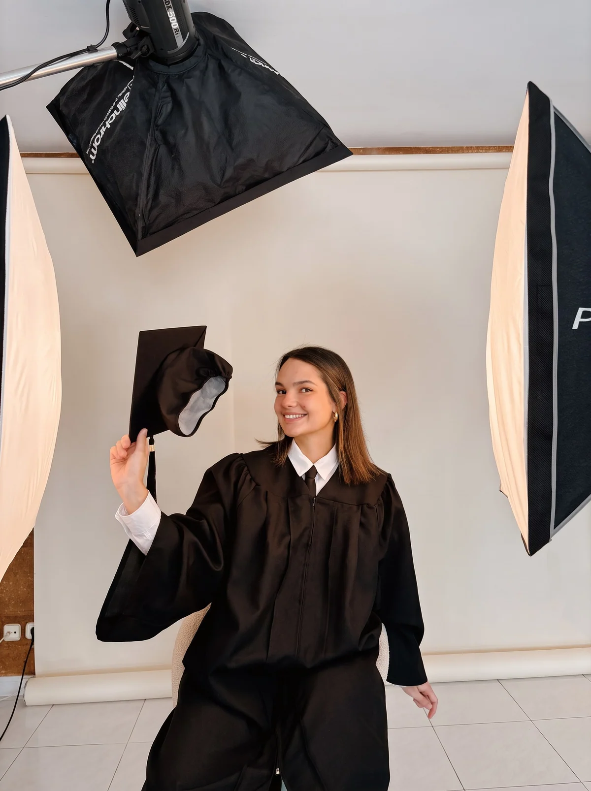 Una graduada levanta el birrete y sonríe entre los focos durante su sesión