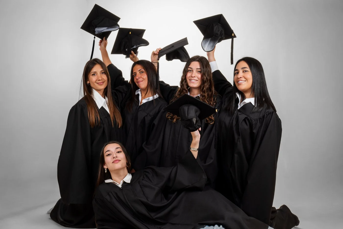 Cinco graduadas con toga levantan el birrete en el estudio