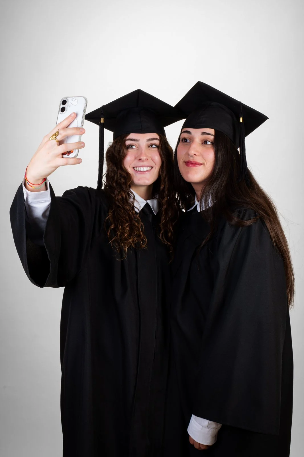 Dos graduadas con toga y birrete se hacen un selfie en el estudio